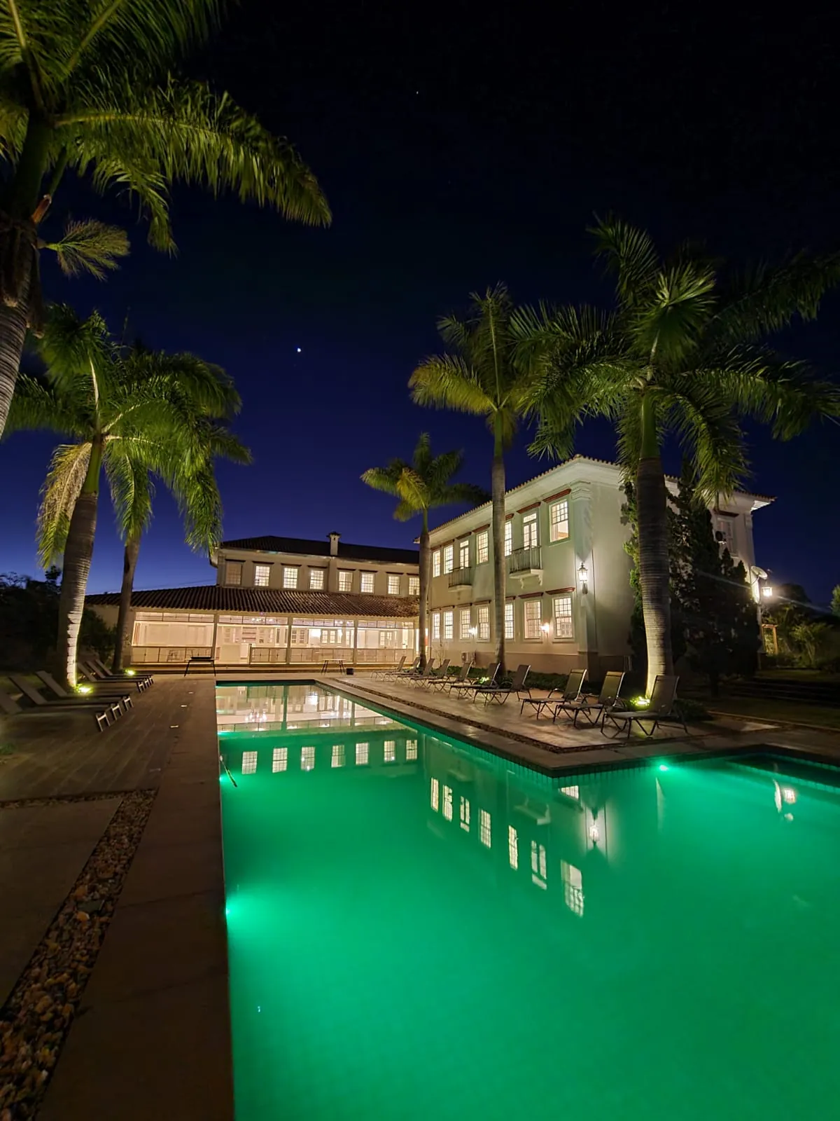 Piscina iluminada à noite entre palmeiras na Inconfidentes Hotel Boutique